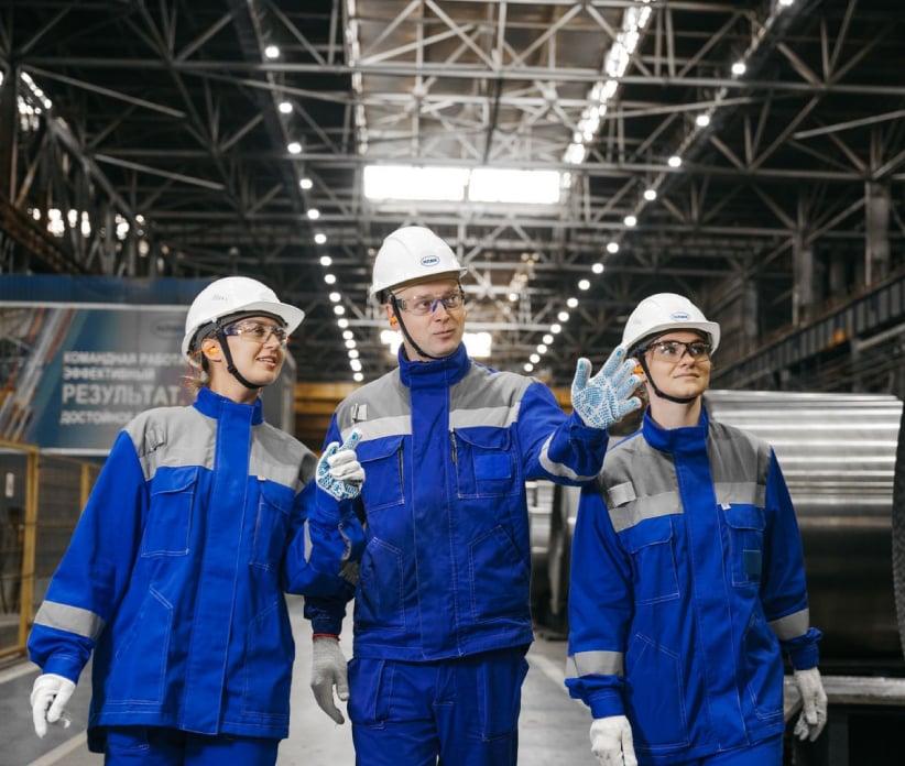 Drei Fachkräfte in Arbeitskleidung und Schutzhelm in einer Industriehalle