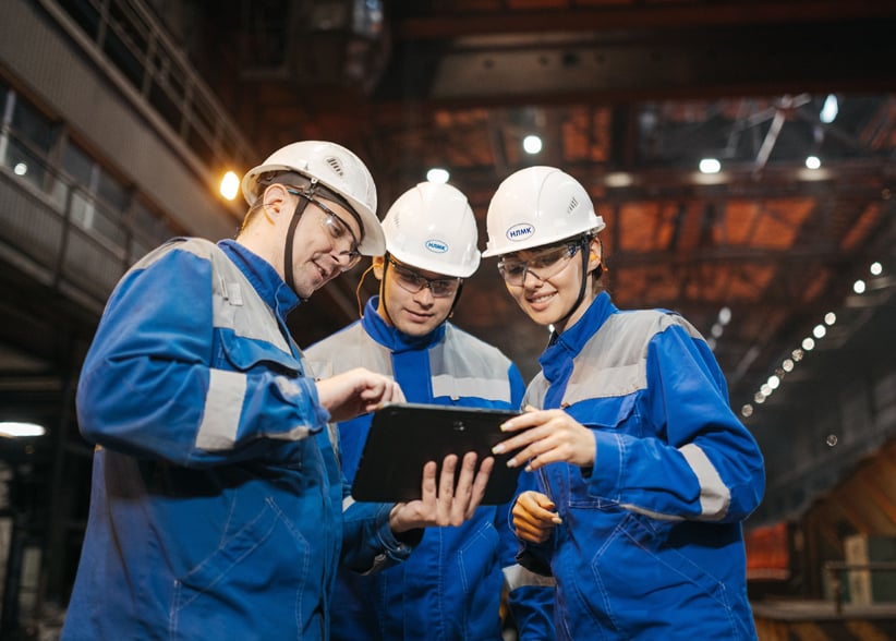 Drei Techniker mit Schutzhelmen besprechen sich an einem Tablet